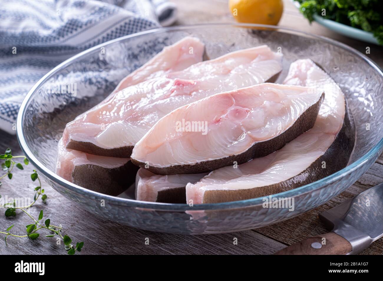 Fresh halibut steaks in a glass bowl on a rustic wood table top. Stock Photo