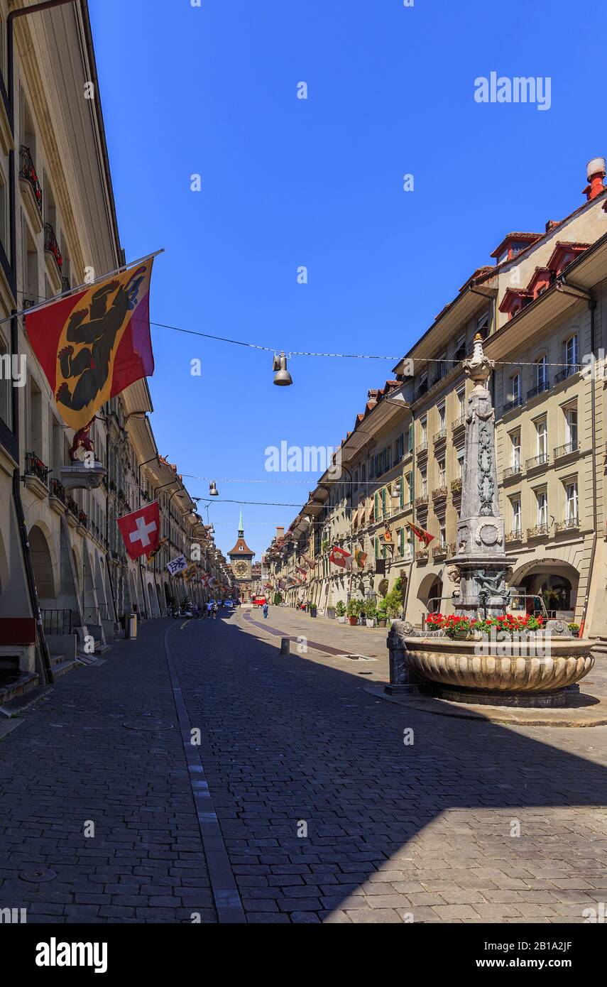 Kramgasse street in the old city of Bern, with the beautiful rusty fountain, red flowers and many flags Stock Photo