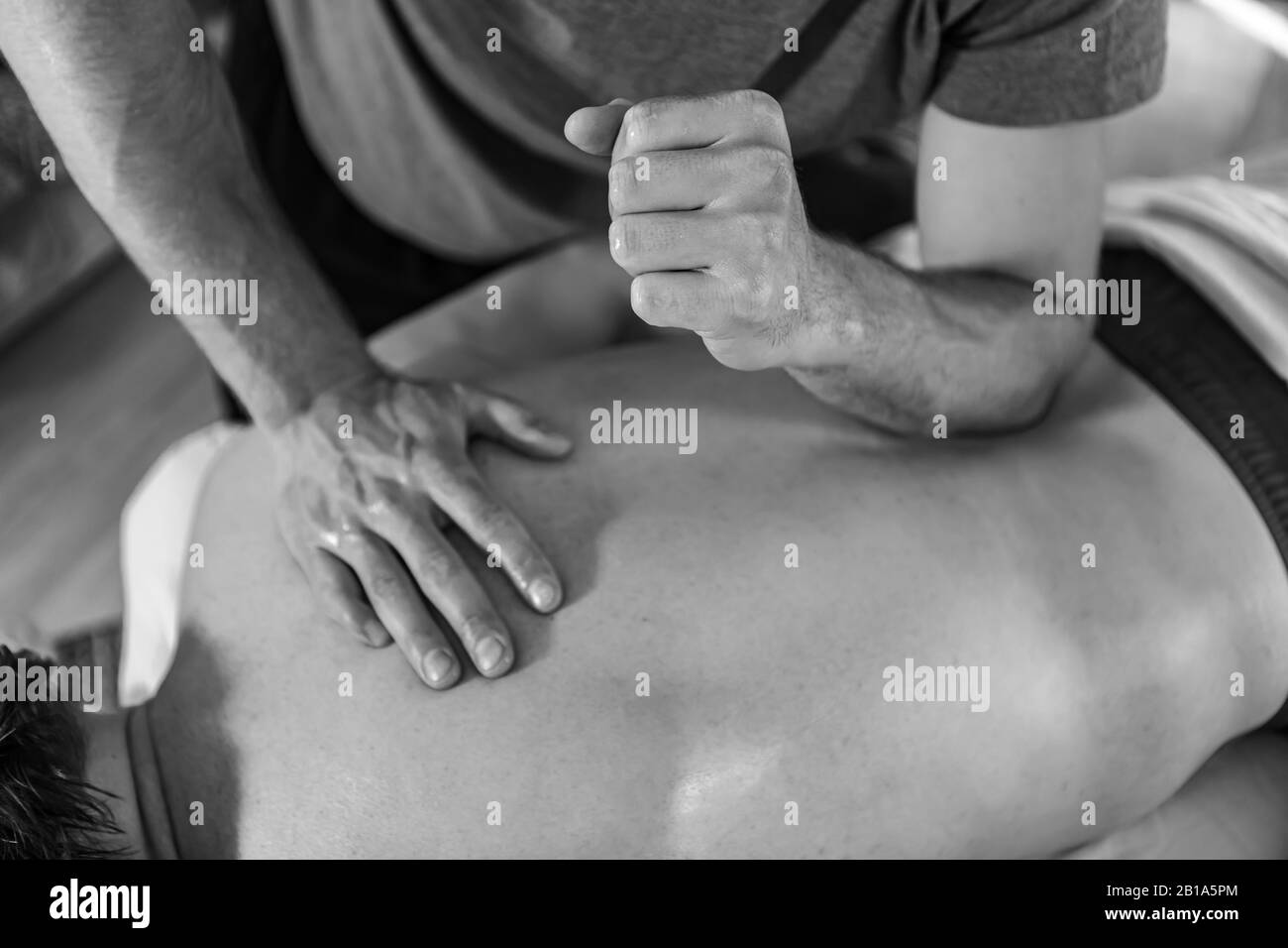 A young sports massage therapist applying pressure with the elbow. Therapeutic body massage treatment. Black and white toned image Stock Photo
