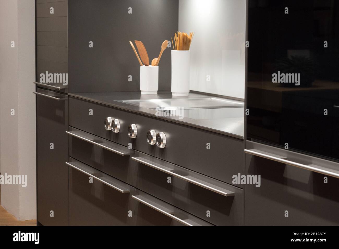Sleek Modern Kitchen with dark surfaces, white utensils and digital display control dials Stock Photo