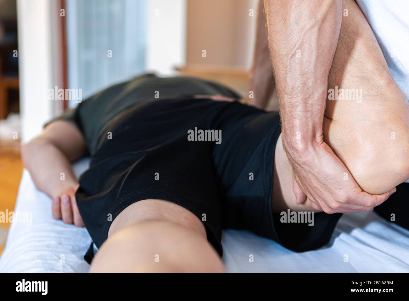 A middle-aged male getting a relaxing leg massage after hard work and training at the gym. Close-up view of masseur hands giving massage therapy Stock Photo
