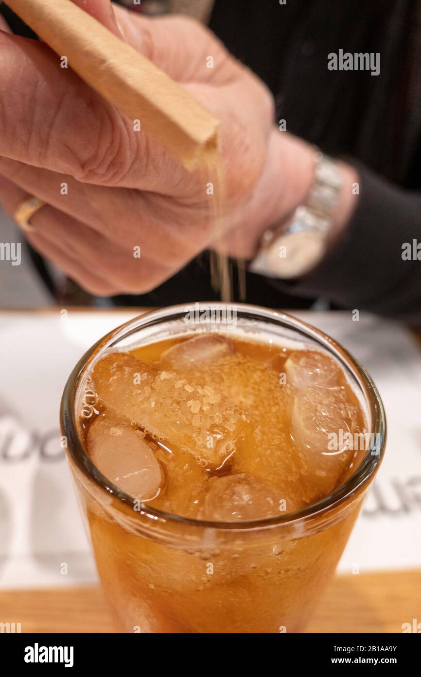 Man adding Sugar to a Glass of unsweetened Iced Tea with Lemon Wedge Stock Photo
