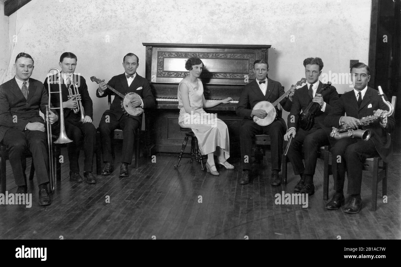 Jazz Band of one woman and six men. Posed with 2 banjos, piano, trumpet, trombone, violin, saxophone.   To see my related vintage images, Search:  Prestor  vintage  music Stock Photo