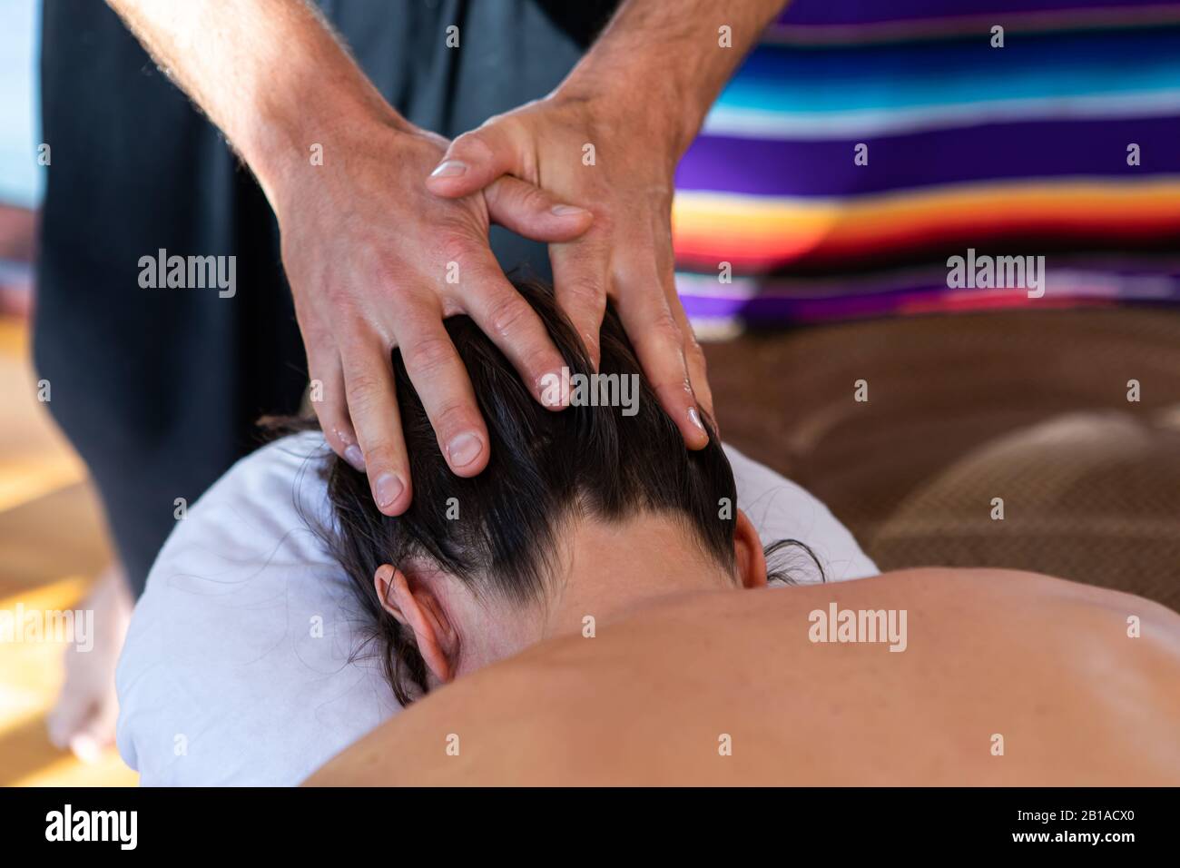 Young woman receiving a head massage in a cosy home environment. A professional masseur giving relaxing massage therapy to spa client Stock Photo