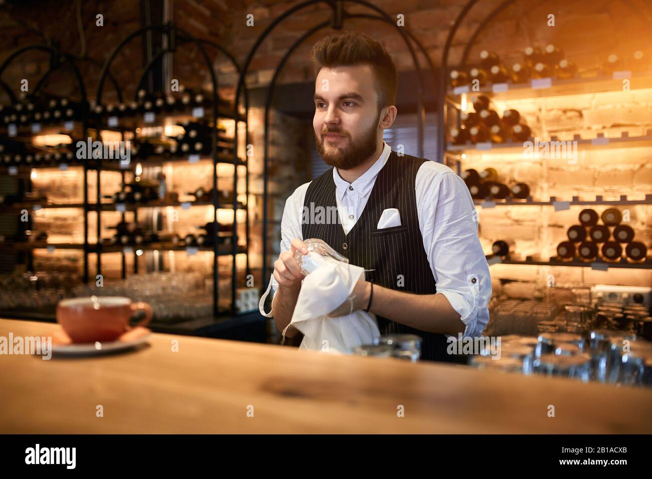 handsome bearded bartender wipes a glass. close up side view photo