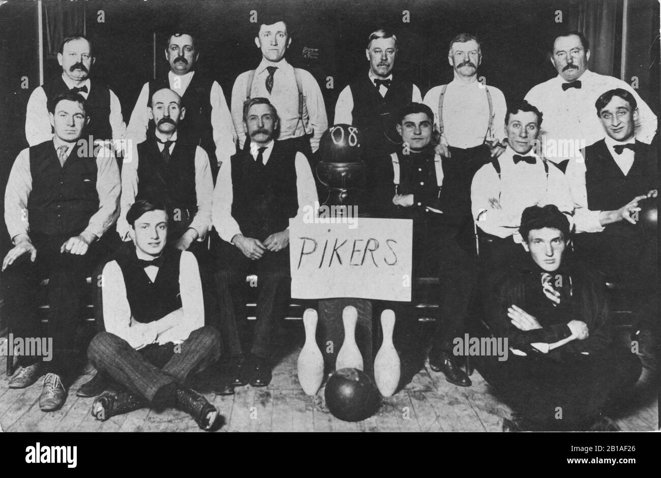 Bowling team, the 'Pikers' in 1908, in Milwaukee, Wis. This is 14 men around three pins, their team name and the bowlers' end of the ball return. There ar 3 bowling balls in the photo.  Men are all dressed in black and white, some with suspenders. Many mustaches on serious faces.  To see my other sports-related vintage images, Search:  Prestor  vintage  sport Stock Photo