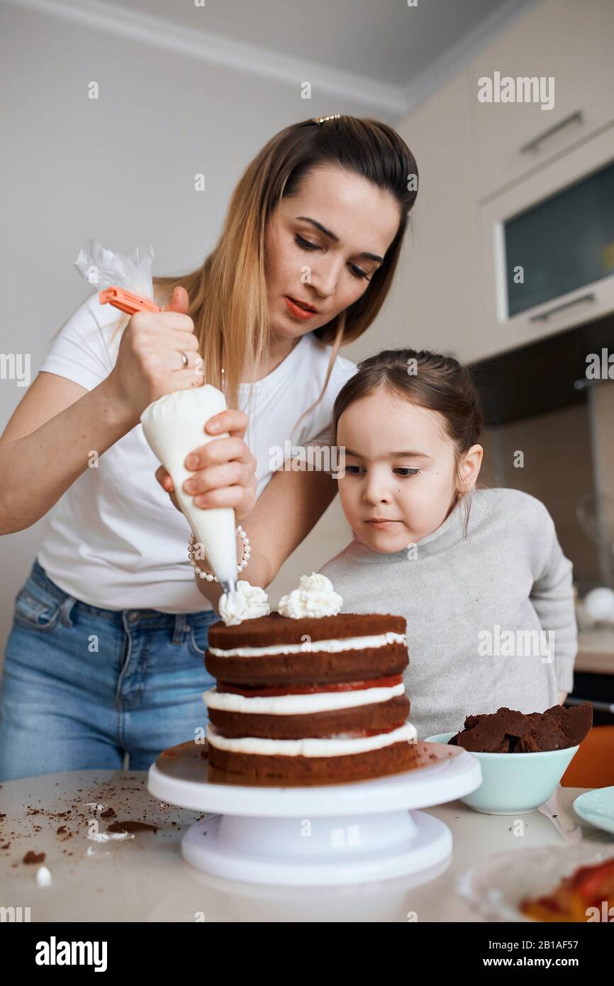 young awesome woman and little girl learning to decorate cake, people