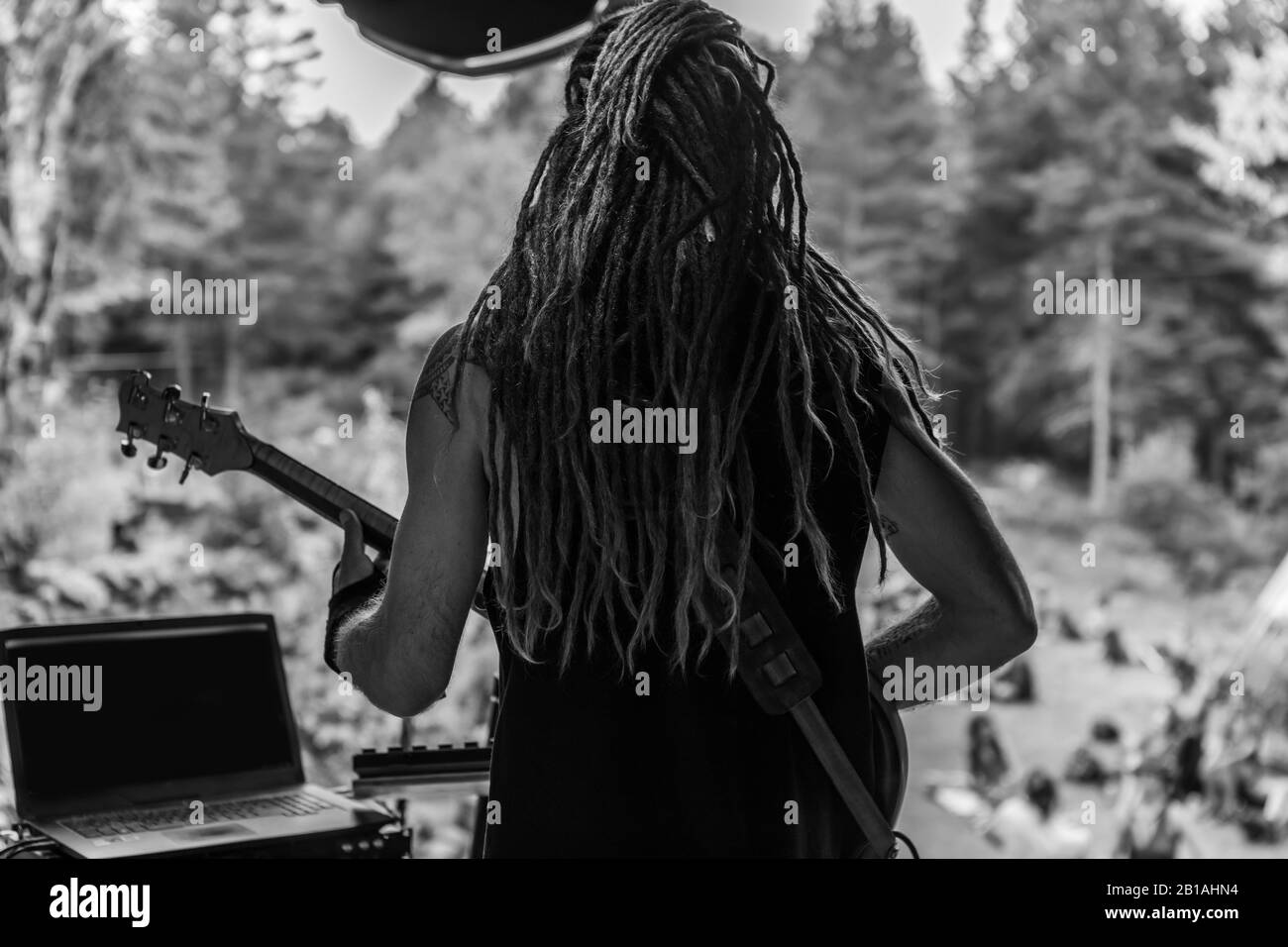 An atmospheric black and white selective focus shot of a guitar player with dreadlocks performing on stage during a multicultural music festival Stock Photo
