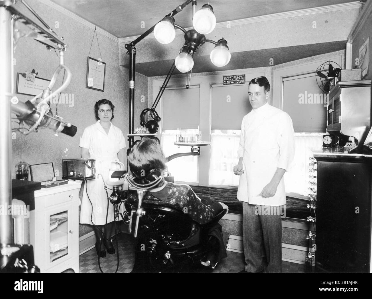 A dental office with the dentist, the woman dental assistant, and all equipment, c. 1925.  Shows the full layout of his medical practice workspace.  To see my other dental-related vintage images, Search:  Prestor  vintage  dental Stock Photo