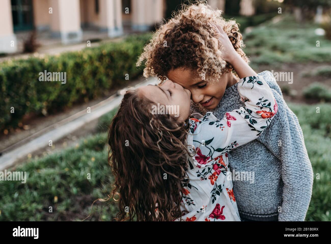 Twin brother kissing sisters cheek while standing outside at park Stock Photo
