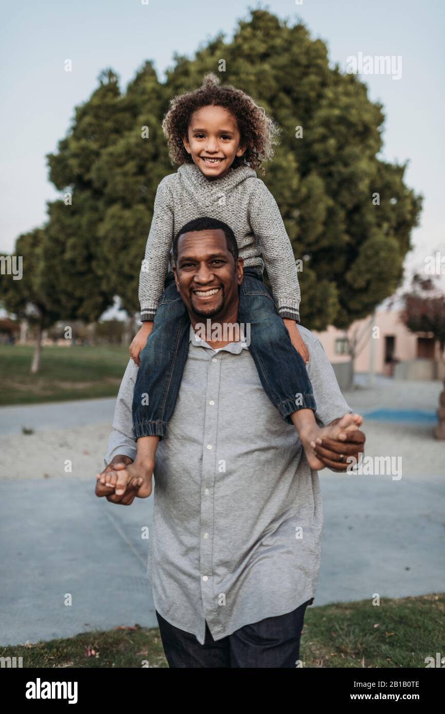Joyful son sitting on happy father's shoulders at park playground Stock Photo