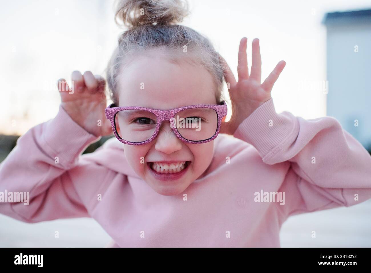 Portrait of a young girl pulling funny faces with pink sparkly glasses Stock Photo