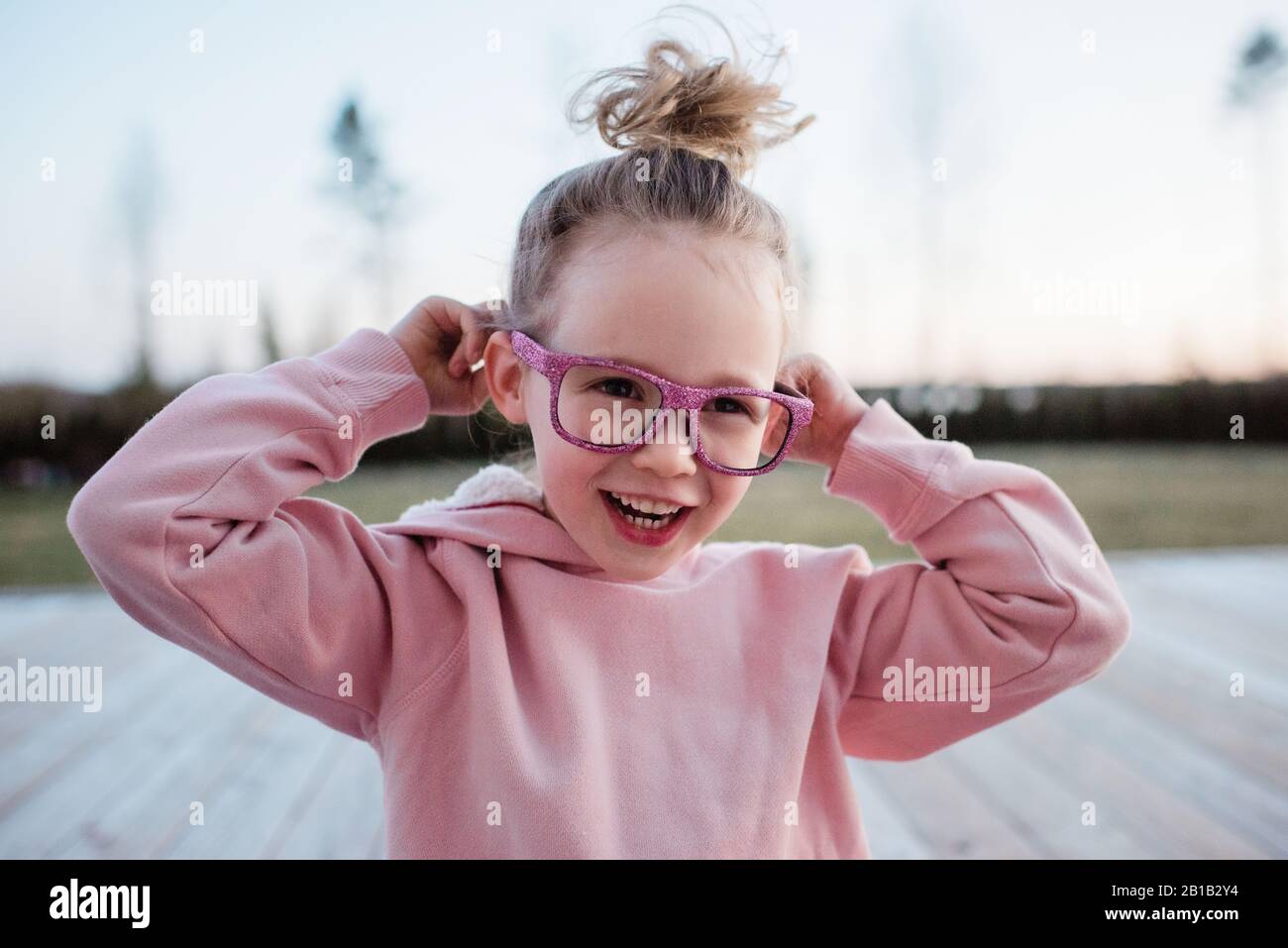 portrait of a young girl pulling silly faces with pink sparkly glasses Stock Photo