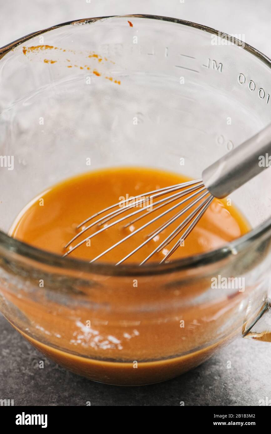 Measuring bowl with marinade and a wire whisk Stock Photo