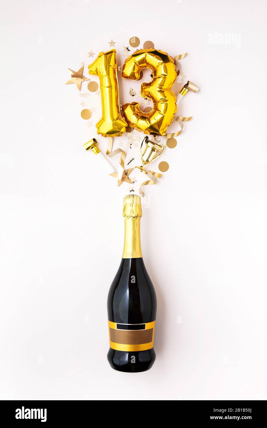 Happy 13th anniversary party. Champagne bottle with gold number balloon. Stock Photo