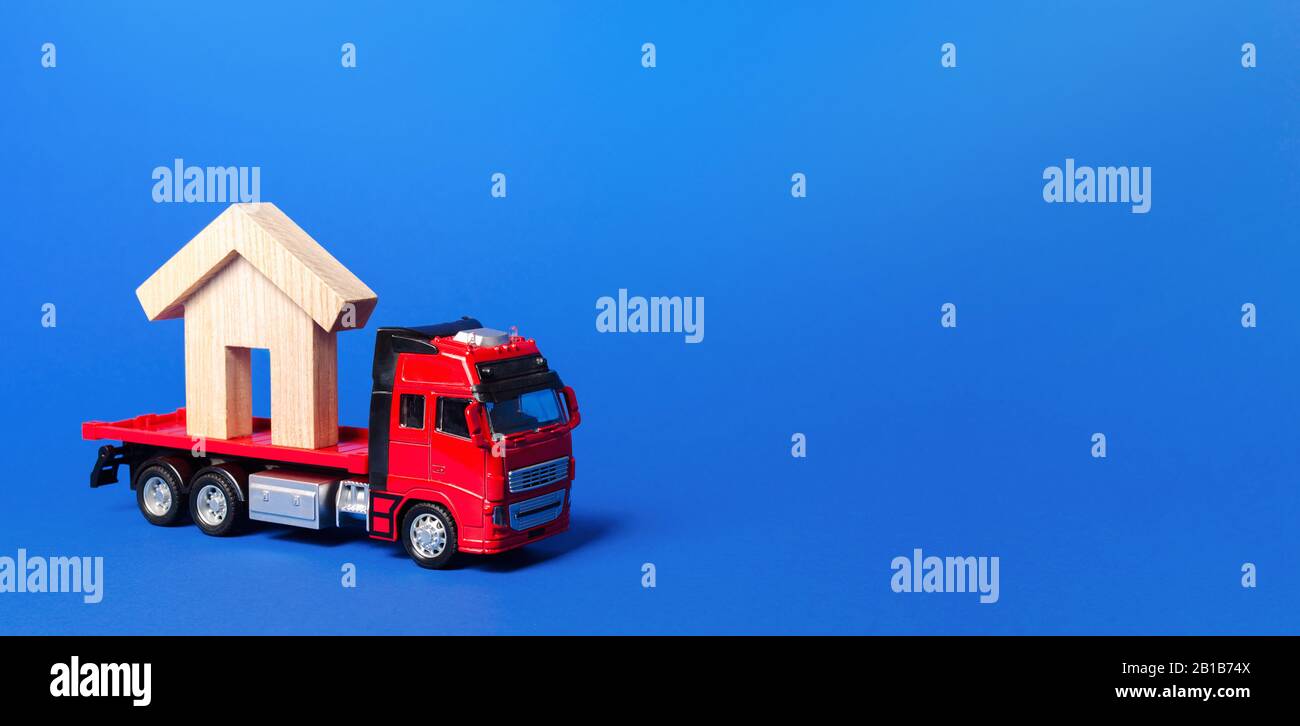 Red truck carrier with a house figure on a blue background. Cargo transportation and delivery service. A moving company. Infrastructure and logistics Stock Photo