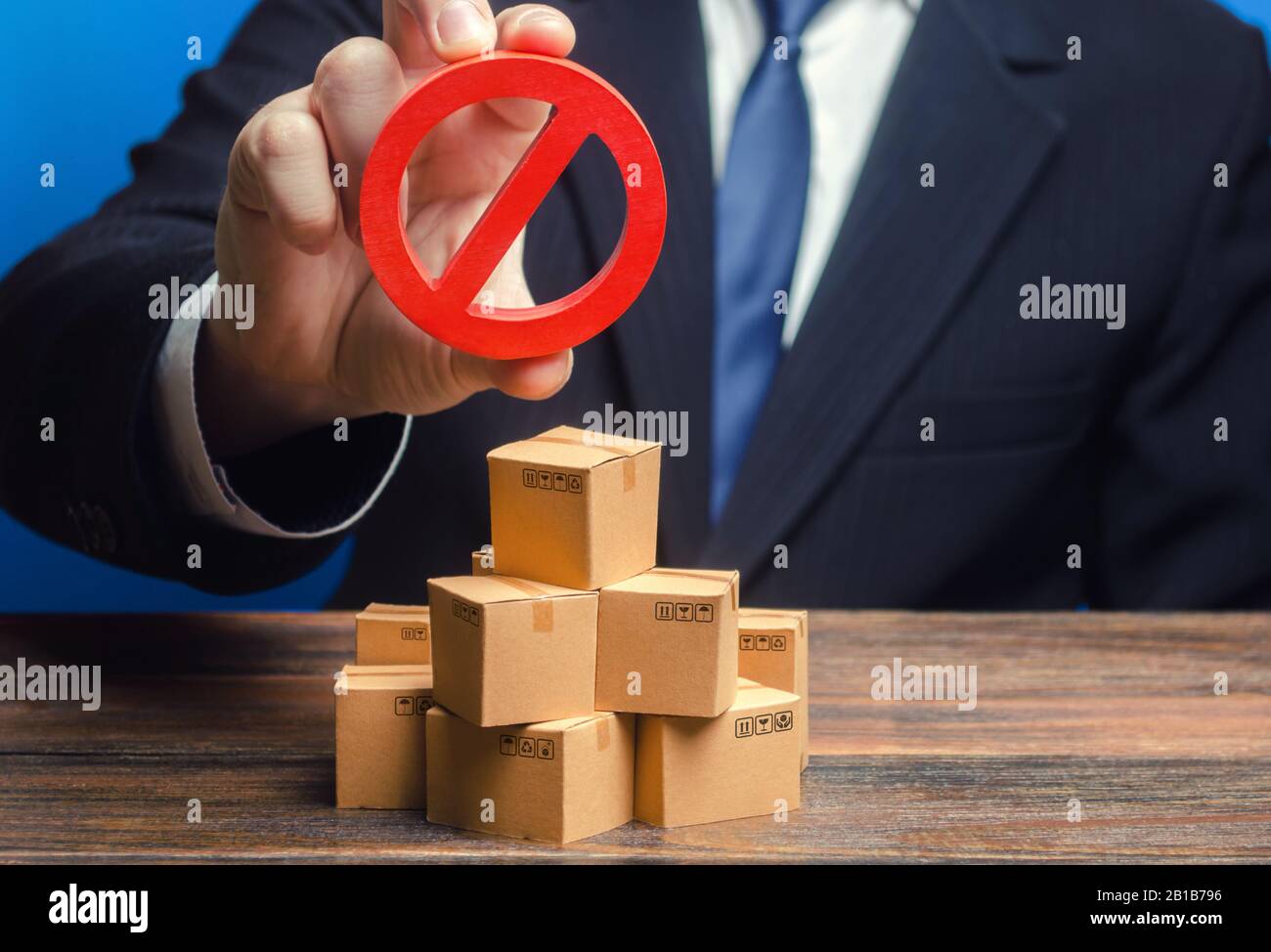Businessman man official holding red prohibition sign NO over boxes with goods. Out of stock. Embargo trade wars. Restriction import, ban export of du Stock Photo