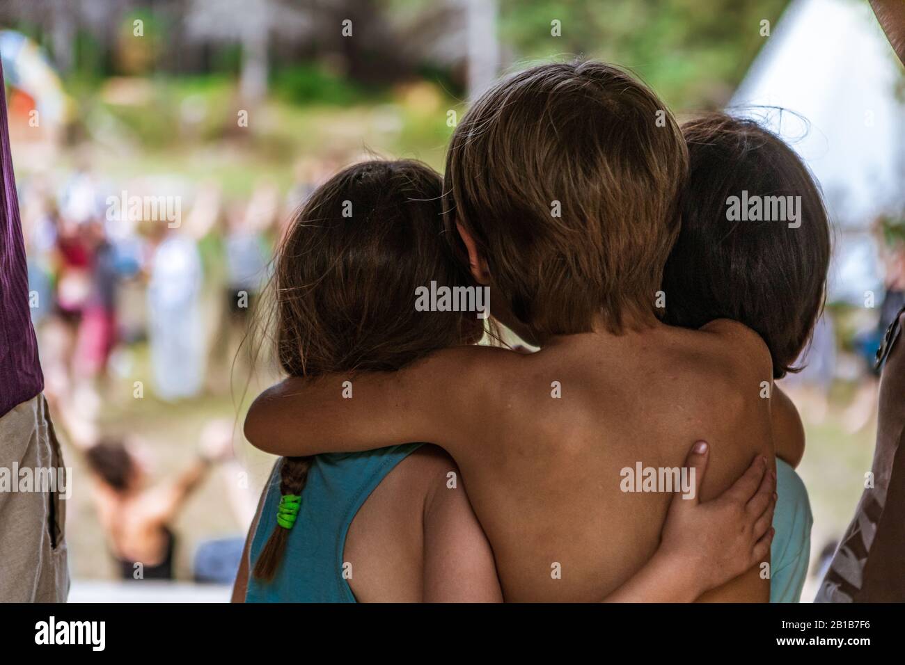 A close up and rear view of three cute children, two brothers and one sister, hugging on stage during a festival celebrating earth and culture. Selective focus shot Stock Photo