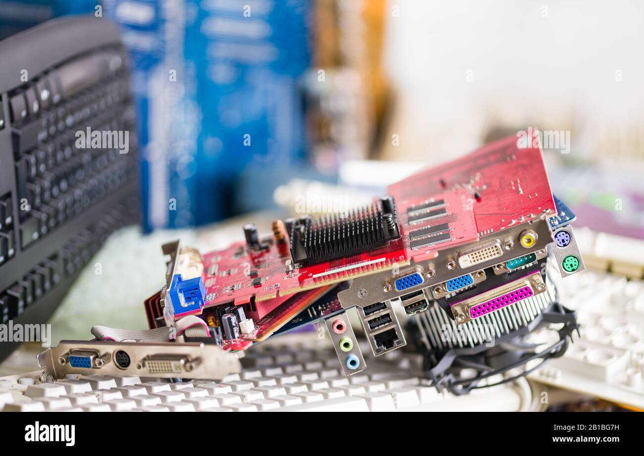 Red computer graphics cards. Electronic waste pile on blurry background. Plastic keyboards, video card, mainboard with colorful connectors and cooler. Stock Photo