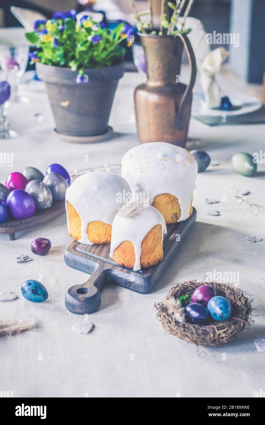 Naturally dyed Easter quail eggs in nest, Easter cakes, fresh violets potted, wooden hearts background, retro styled spring holiday greeting postcard Stock Photo