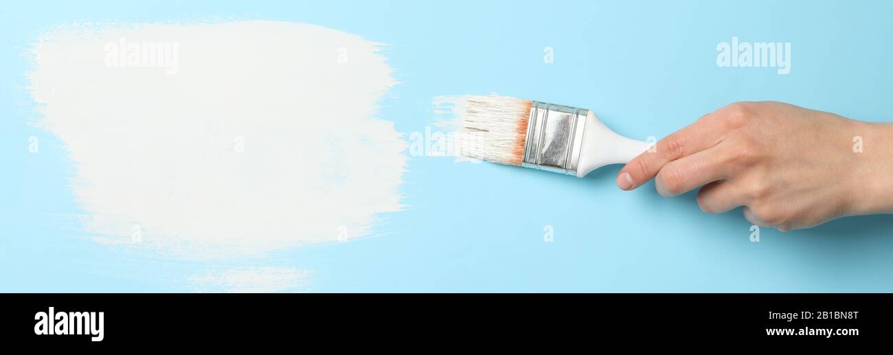 Female hand holding brush on blue background with white paint strokes ...