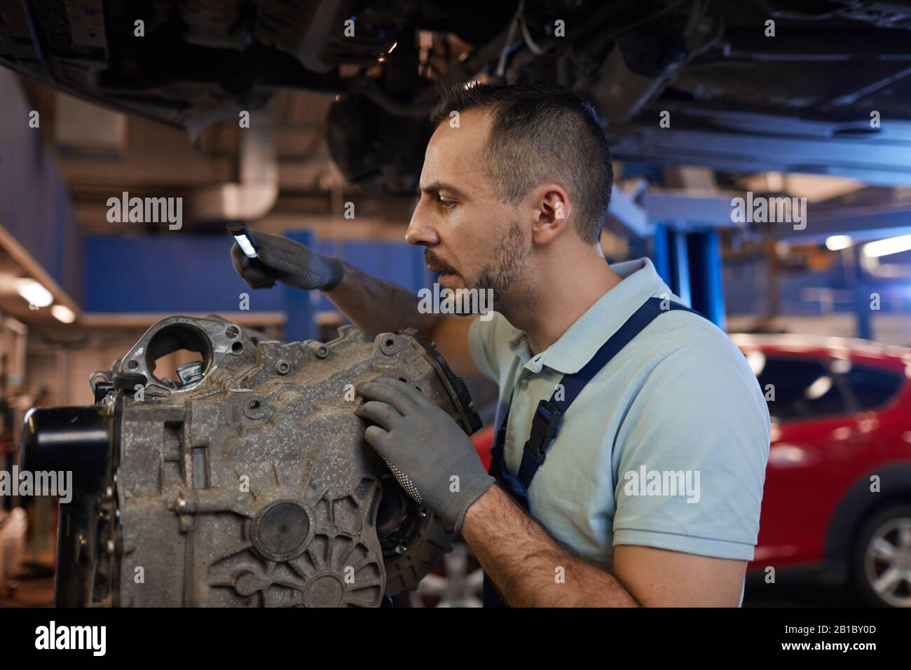 Side view portrait of car mechanic inspecting gearbox in auto repair