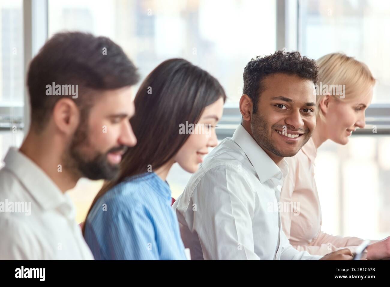 Indian black man sitting amoung colleagues smiling. Stock Photo