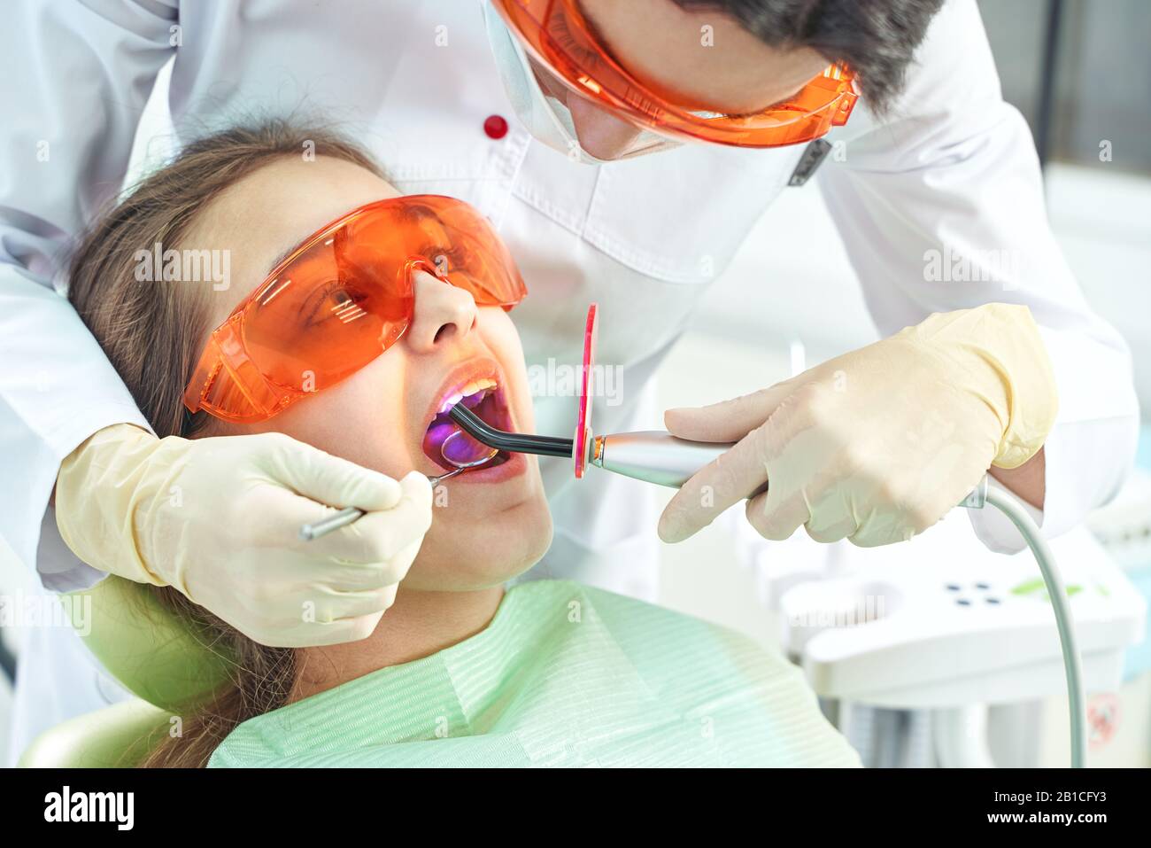 Girl child at the doctor. Dentist places a filling on a tooth with dental polymerization lamp in