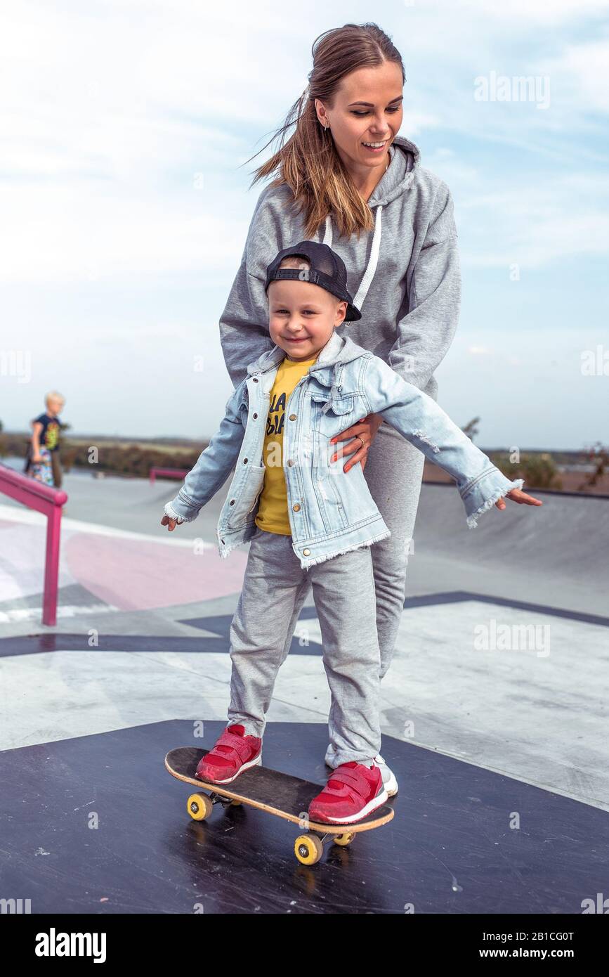 Woman mom, holds little boy son 3-5 years old, learning to ride a skateboard,  in the summer on the sports ground, emotions of happiness, fun Stock Photo  - Alamy