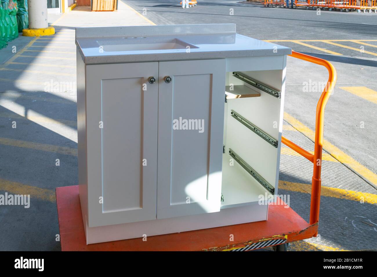 A white cabinet with the drawers removed sits on a trolley cart outside a home improvement store. Stock Photo