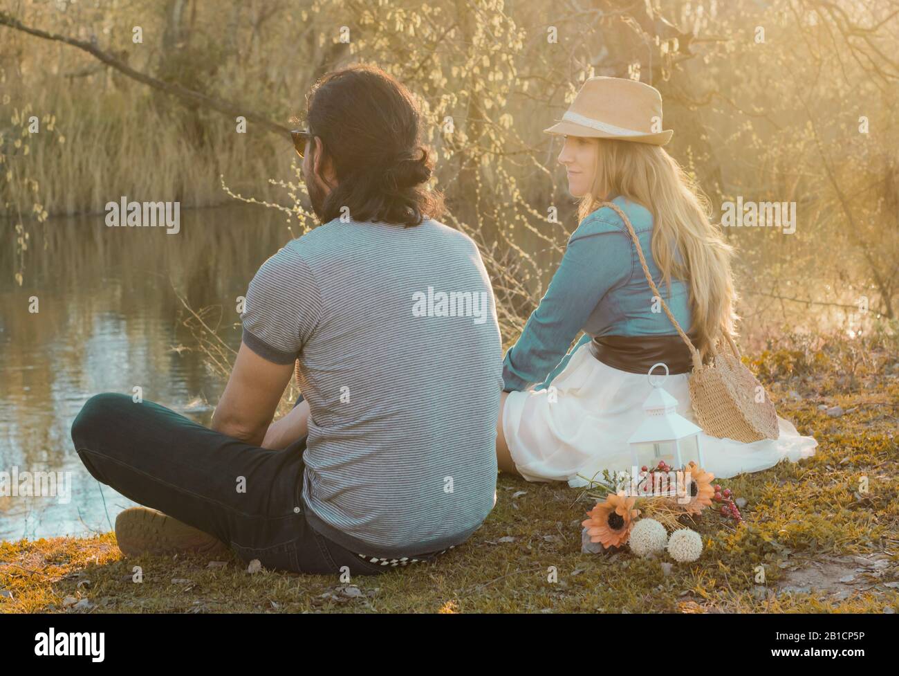 Young couple sitting on the grass in front of the river at sunset. Human relationships, positive emotions Stock Photo