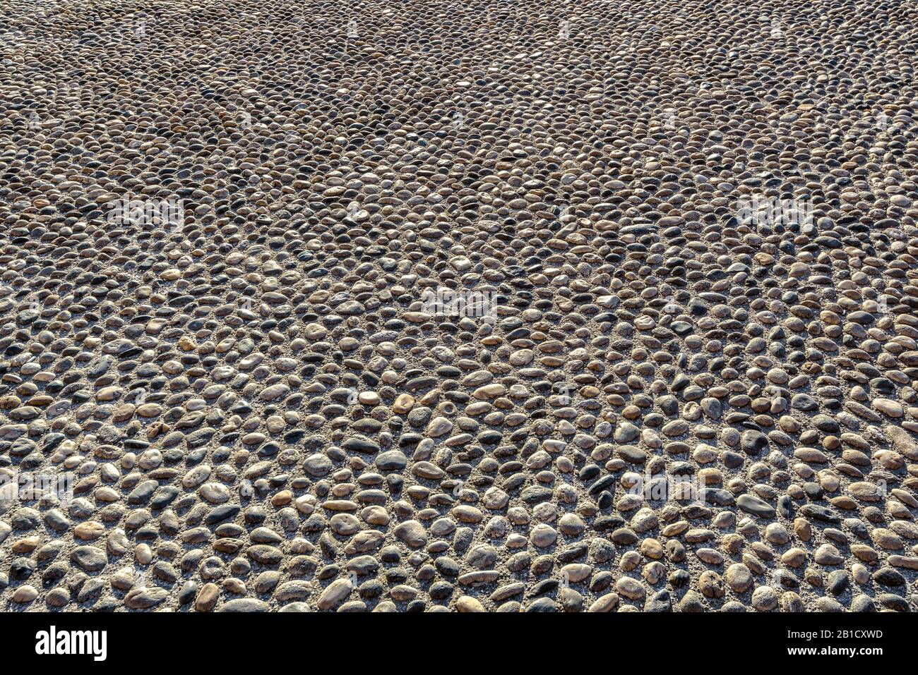 Cobblestone road background. Stone pavement in perspective. Old street paved with rocks. Paving ground close-up in summer. Texture of floor with pebbl Stock Photo