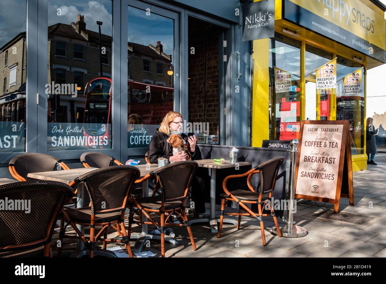 Woman with her dog enjoys a break at an urban patio of a cafe on Chiswick High Street, London, England Stock Photo