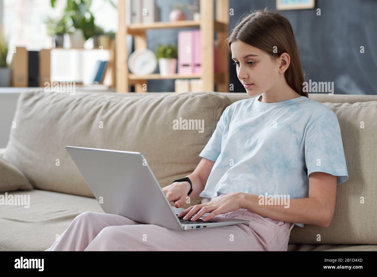 Serious teenage girl sitting on sofa at home and using laptop while ...