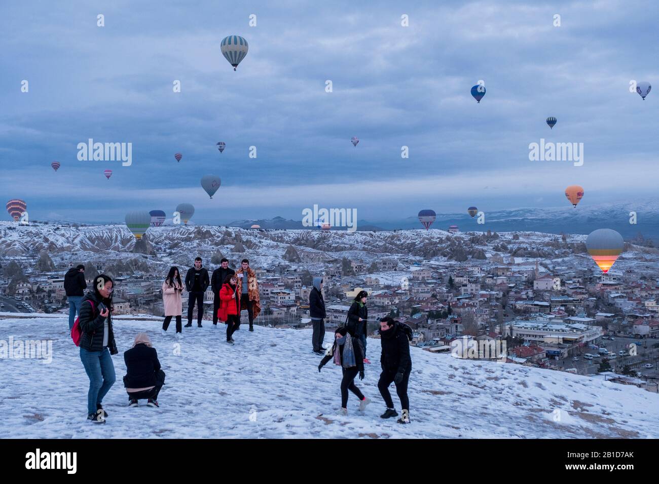 Cappadocia in winter covered with snow, tourists and hot-air balloon taking off near Göreme Stock Photo