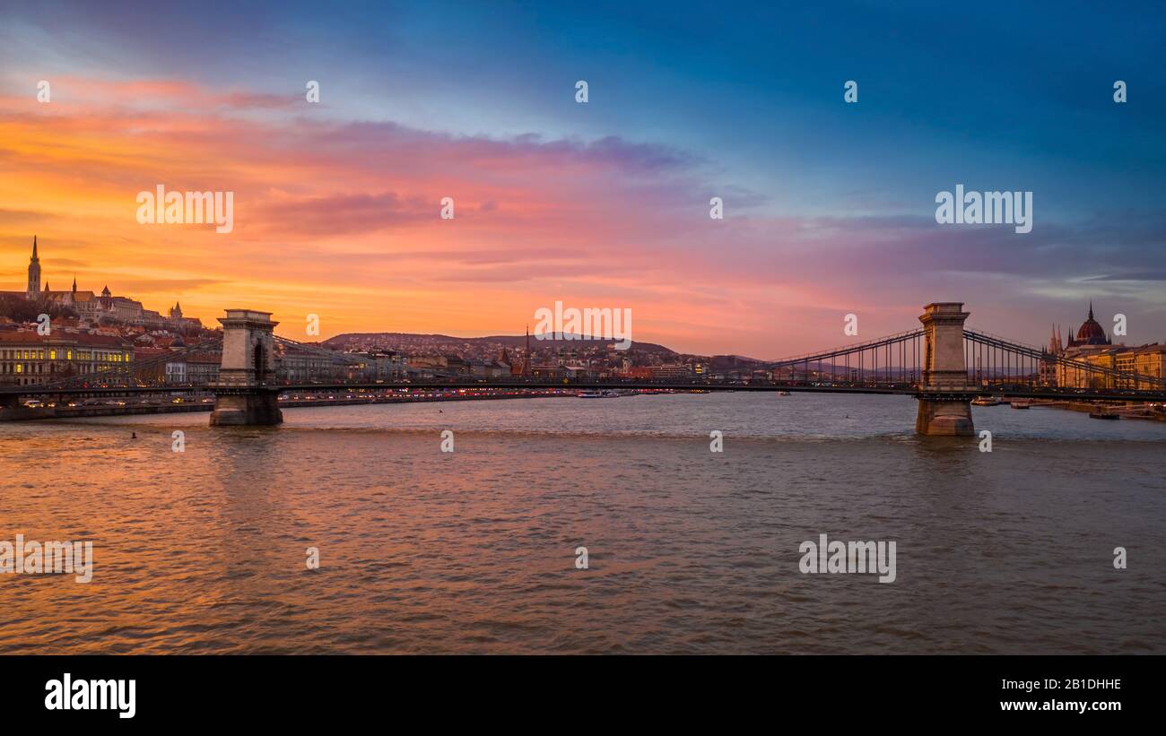 Budapest, Hungary - Aerial view of the famous Szechenyi Chain Bridge with a beautiful golden sunset at winter time. Matthias Church and Parliament at Stock Photo