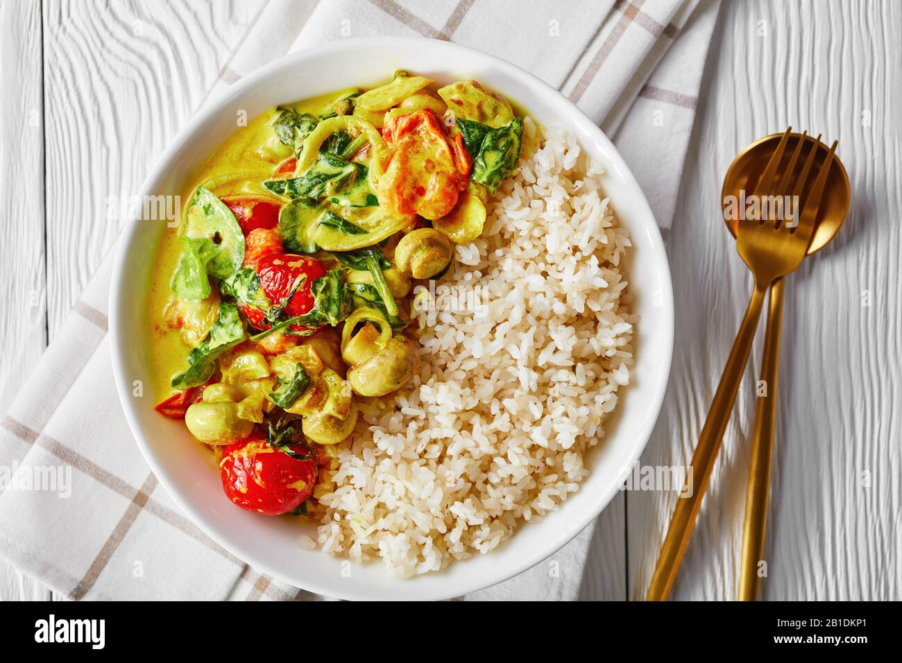 Vegan meal coconut and mushroom curry with fresh spinach, cherry tomatoes  served with rice on a white plate with golden cutlery on a white wooden  tabl Stock Photo - Alamy