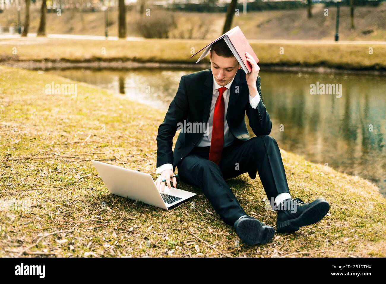 young guy tired of work. man in a suit running on the nature near the lake. Generations Y, millennials Stock Photo