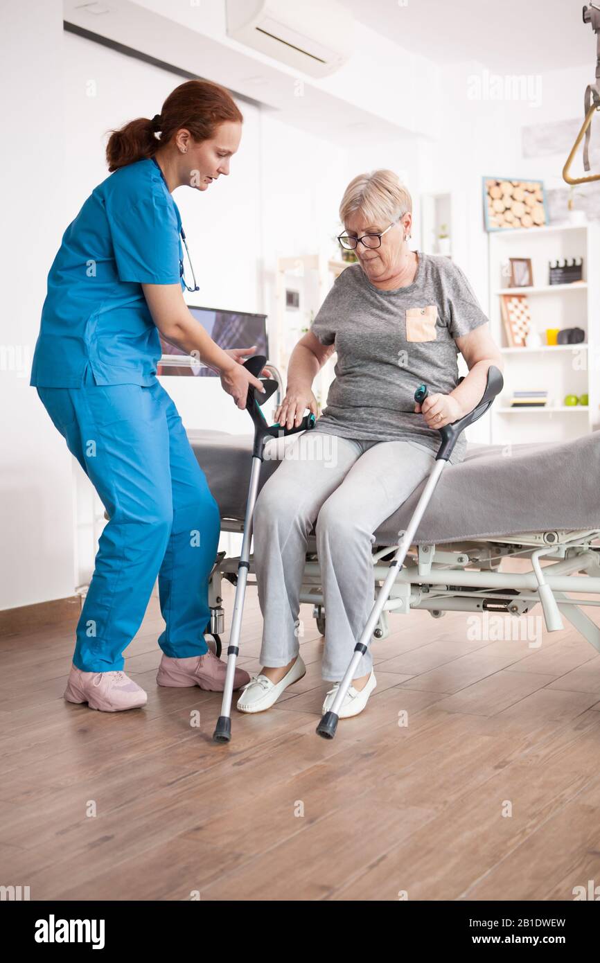 Nurse helping old woman to sit on bed in nursing home after walking