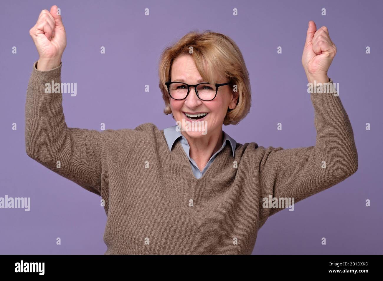 Mature senior woman doing a winner gesture holding fists up enjoying the moment on a colored background Stock Photo