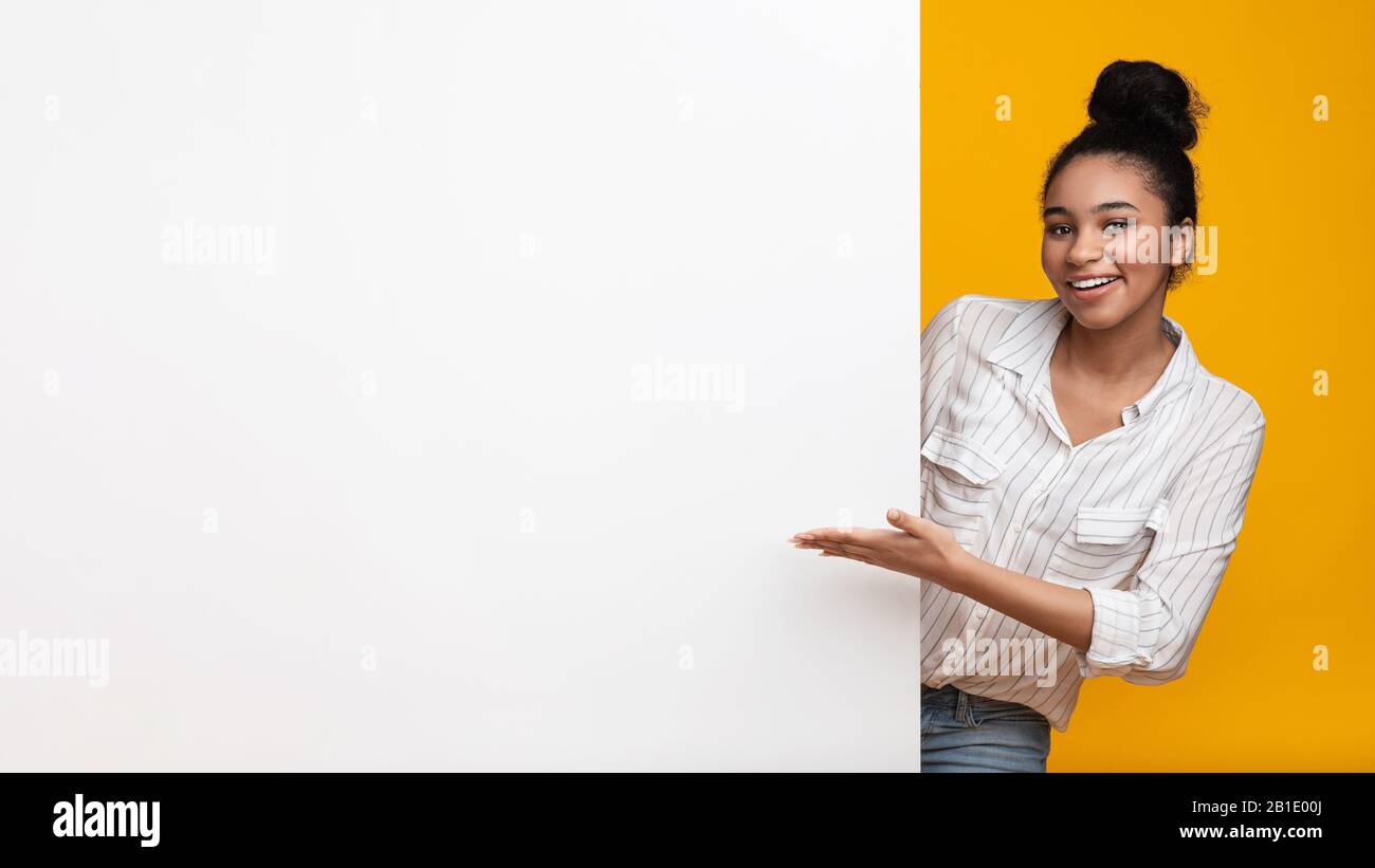 Smiling afro woman pointing at blank advertisement board with open hand Stock Photo
