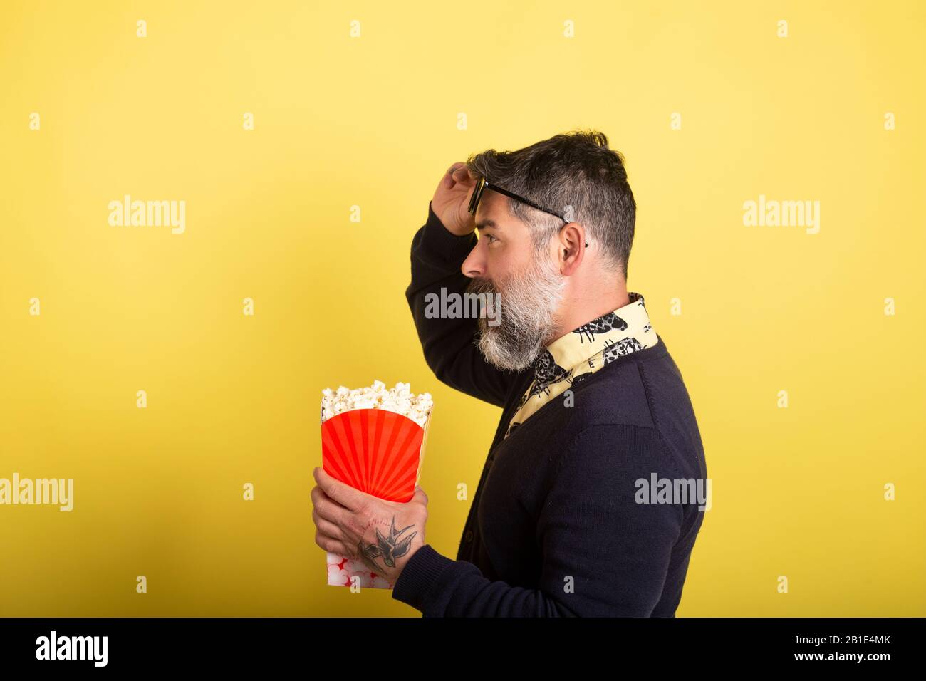 Handsome man with camera profile sunglasses holding a box full of popcorn on yellow background. Stock Photo