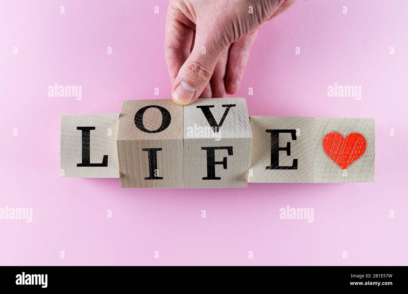 hand turning wooden toy blocks with words LOVE LIFE and red heart symbol on pink packground Stock Photo