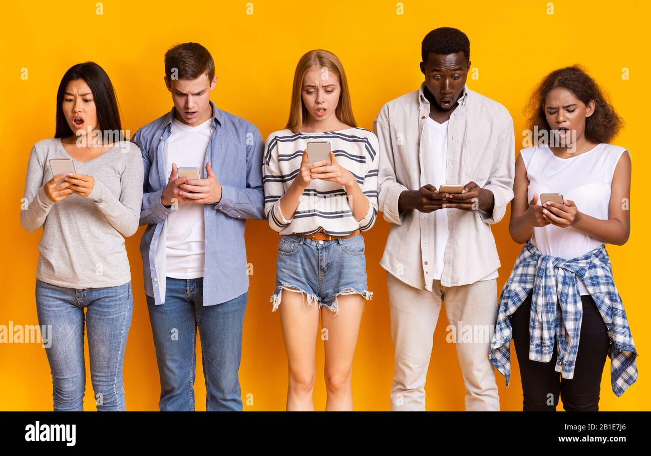 Young friends staying in row, using smartphones Stock Photo
