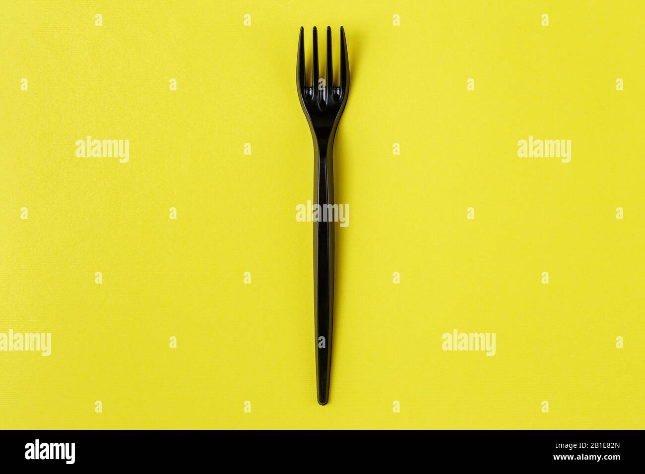 Black plastic fork on yellow background. plastic pollution Stock Photo