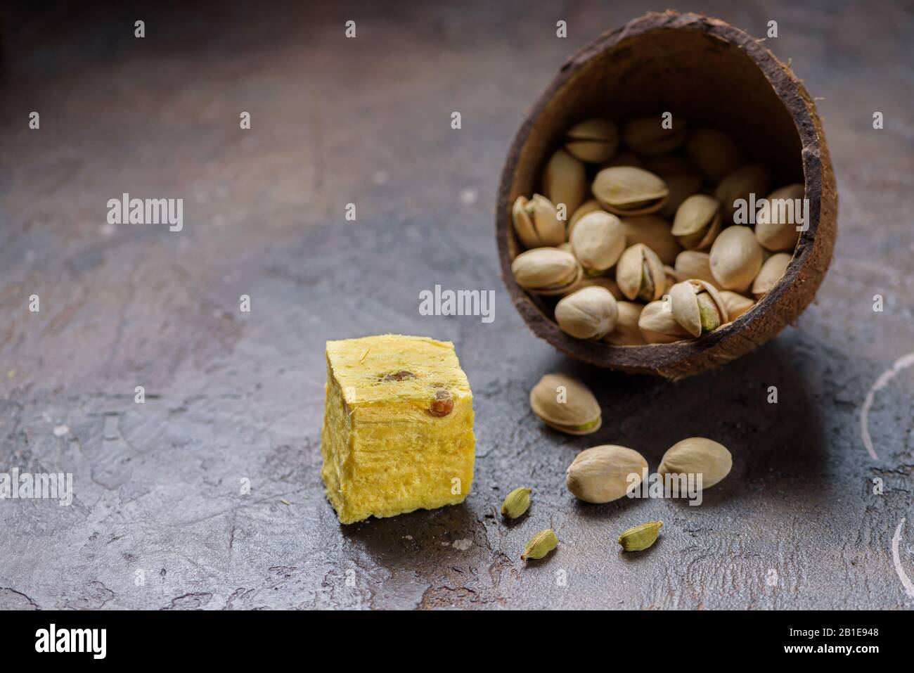 One cube of dessert soan papdi, cardamom grains and pistachios on concrete kitchen worktop.. Stock Photo