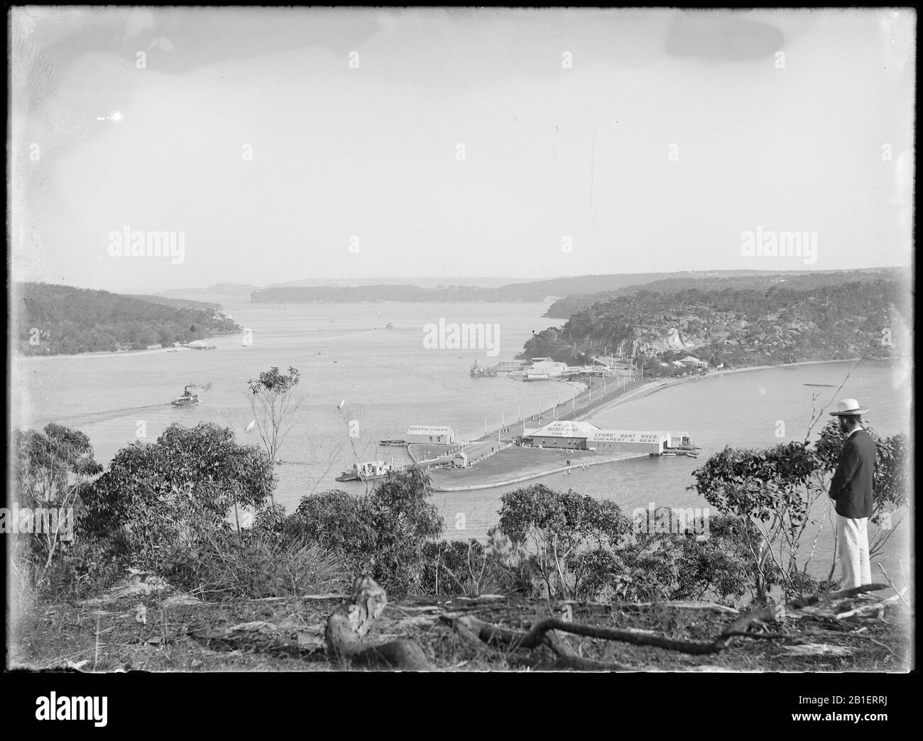 [Macpherson] male on hillside overlooking Spit with punt at mooring behind and view to A. McKayes Refreshment Rooms, Lyons Boatshed in the distance by State Li 0322 Stock Photo