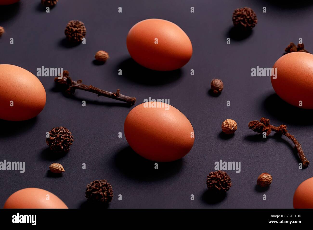 Pattern made of natural brown eggs, dry tree cones and seeds on dark background. Minimal food and Easter concept. Stock Photo