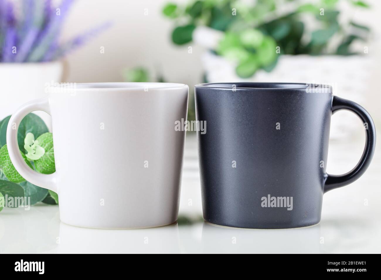 White and black mugs on a background of flowers . Mock up. Template Space for Creative Artwork Lettering Text Product Promotion Branding. Elegant Stock Photo