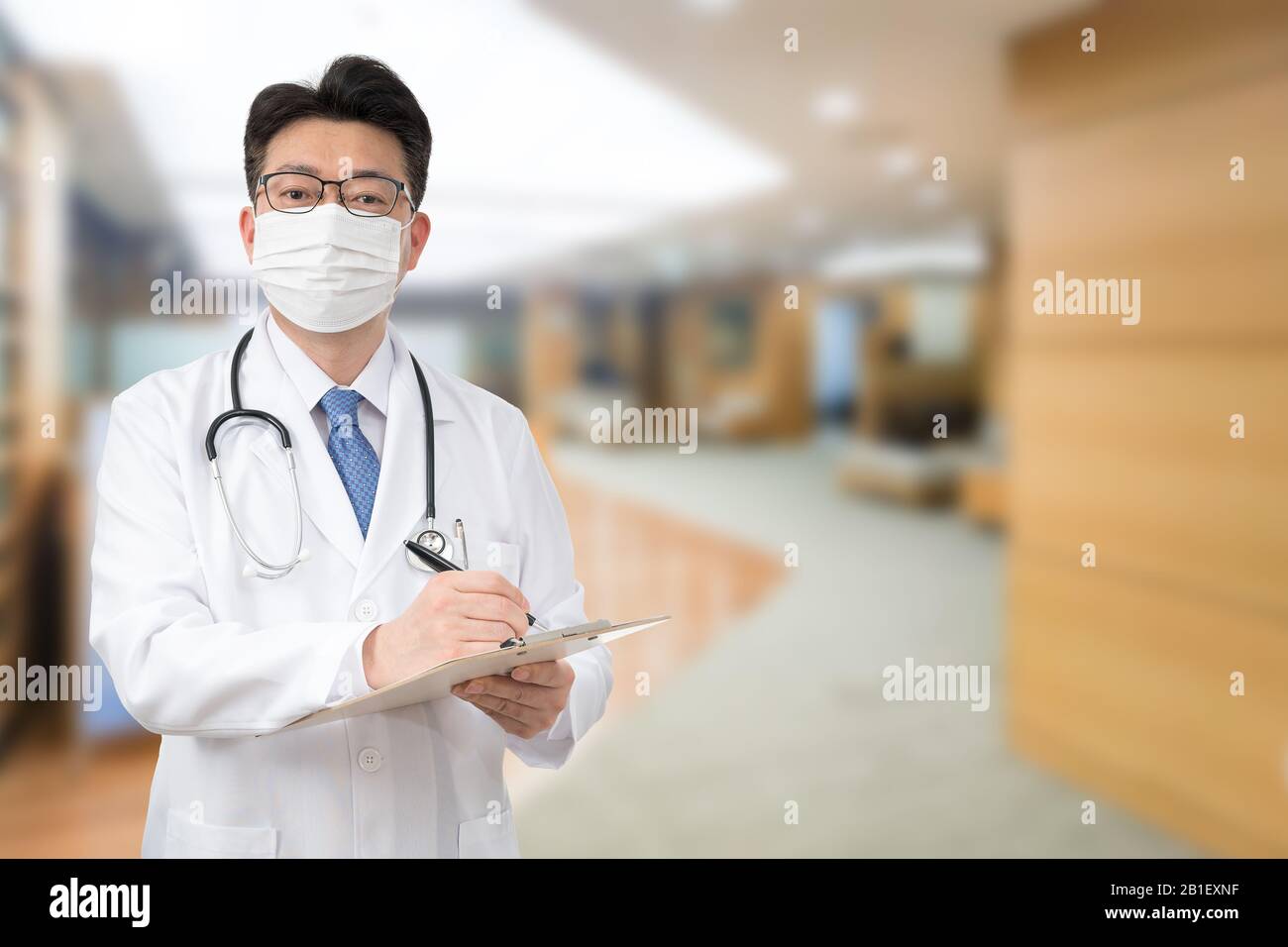 An Asian male doctor holding a medical chart at the hospital while wearing a mask Stock Photo